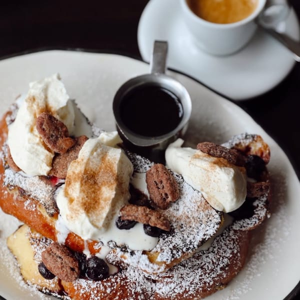 French toast with whipped cream, pecans, blueberries, powdered sugar, and a side of syrup and coffee.
