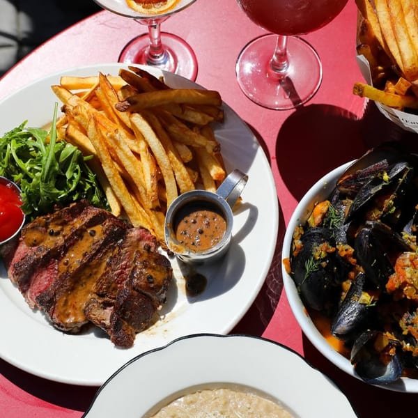French steak frites with peppercorn sauce, mussels, and cocktails on a red table.