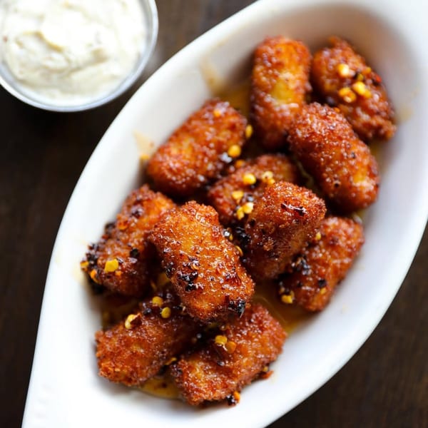 Crispy fried banana fritters with chili flakes and honey, served with a side of cream.
