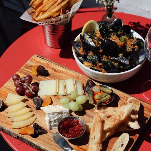 A French charcuterie board with cheeses, grapes, dried fruit, baguette, and jam, alongside mussels and fries.
