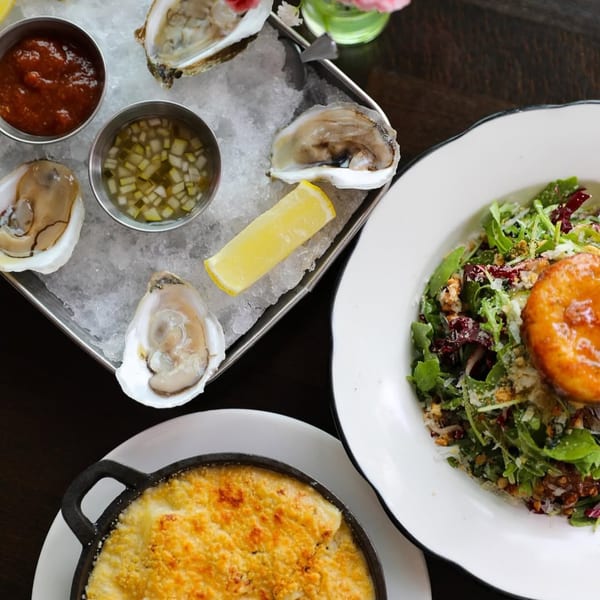 Oysters on ice with sauces, a fresh salad, and a baked dish on a dark table.