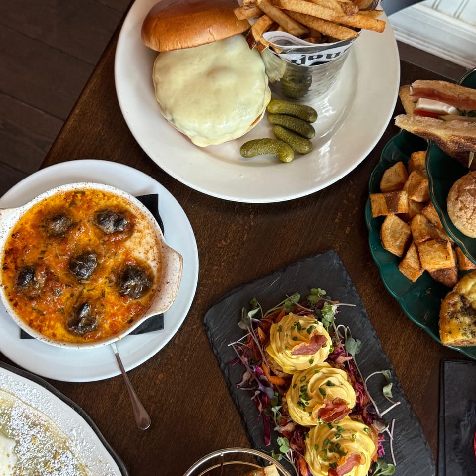 Overhead view of a table laden with French dishes, including escargots, a cheeseburger with fries, and deviled eggs.