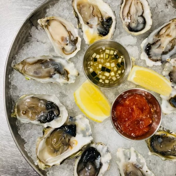 A dozen fresh oysters on a bed of ice with lemon wedges, mignonette, and cocktail sauce.